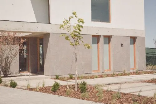 Frente de la casa con un árbol joven y canteros recién plantados sobre mulch