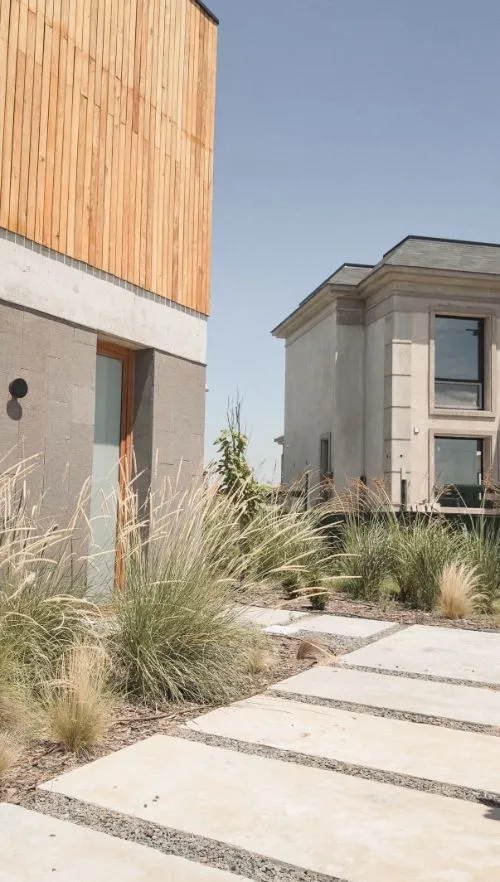 Ingreso con losetas entre gramíneas, junto al revestimiento de madera de la casa