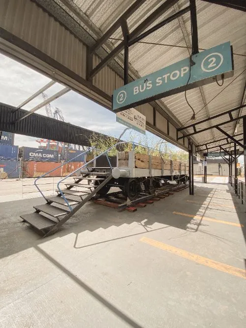 El vagón de carga restaurado con su escalera de acceso, bajo el alero de la terminal de cruceros