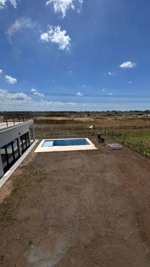 Vista desde la planta alta: el lote sin vegetación, la pileta y el campo abierto detrás del alambrado